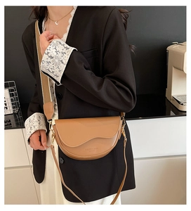 Detail of khaki saddle bag featuring a wide fabric strap and fashion leather embossing