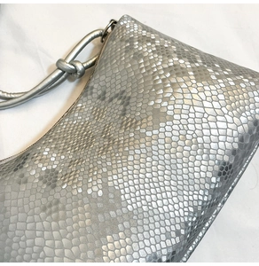 Detail of silver snake-embossed faux leather bag with elegant knotted shoulder strap design