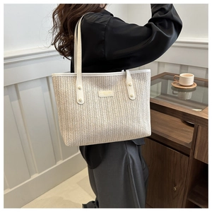 Detail of a cream woven straw tote bag with faux leather handles worn by a model