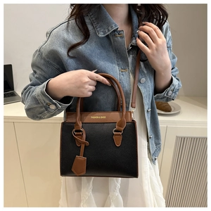 Detail of a two-tone crossbody bag with lychee grain leather and fashion text on a desk
