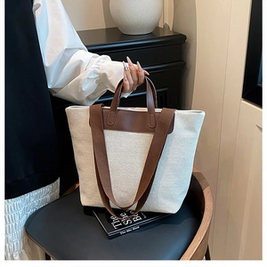 Detail of canvas tote bag featuring brown leather handles and adjustable shoulder strap