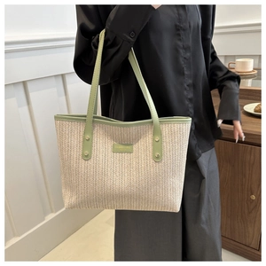 Close-up of woven straw tote bag with green trim and metal logo plate detail