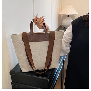 Close-up of beige canvas tote bag with brown leather handles and wide fabric shoulder strap