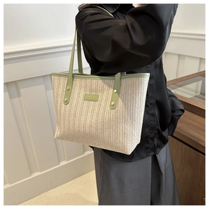 Detail of large woven straw tote bag in beige and green, modeled for lifestyle usage