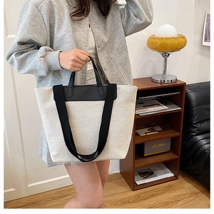 Chic beige canvas tote bag with black leather straps styled in a warm indoor setting
