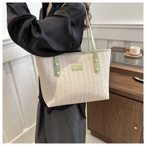 Macro detail of large straw tote bag featuring green leather trim and rivet accents