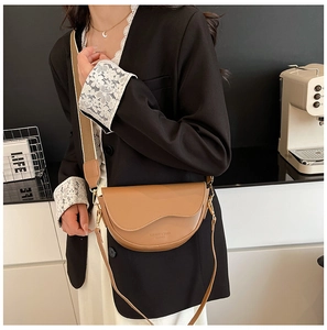 Detailed close-up of brown leather saddle bag with fashion logo and woven wide strap