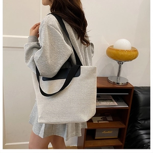 Detail view of a large cream linen tote bag with black straps worn by a model in a room
