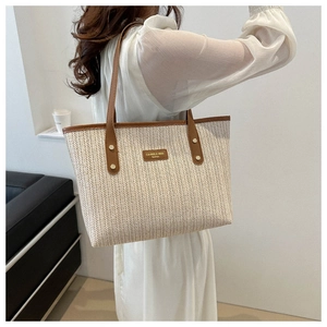 Macro detail of hand-woven straw tote with brown leather trim and golden logo plate