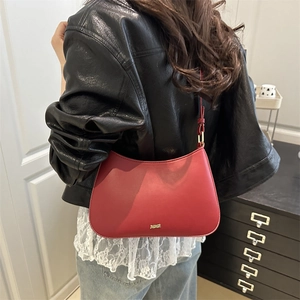 Red leather hobo underarm bag with gold metal logo worn by model in a home setting