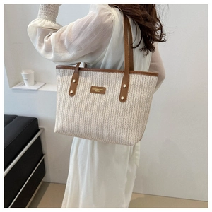 Detail of herringbone straw weave and brown leather trim on a beige tote bag
