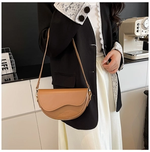 Brown leather saddle bag with wave flap design worn on shoulder over black blazer