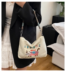 Close-up of cat embroidery and braided rope strap on beige canvas shoulder bag