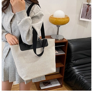 Detail of a large canvas tote bag with black leather accents and woven straps on a sofa