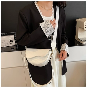 Detail of white saddle bag with scalloped edge flap and wide strap worn by a model
