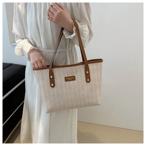 Detail of hand-woven beige tote bag with brown leather handles and brand patch