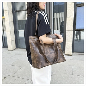 Detail of vintage brown textured leather tote bag carried by model in outdoor setting