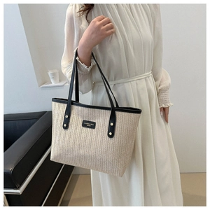 Detail of beige straw tote bag featuring black leather trim and branded metal plaque