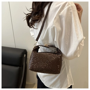 Detail of dark brown faux crocodile leather bag with gold chain and strap on sofa