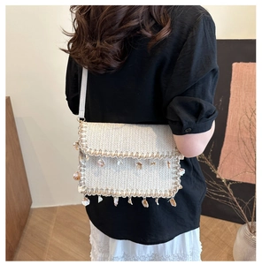 Detail of straw woven crossbody bag with shell charms and bohemian fringe trim
