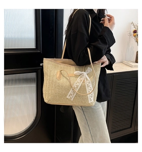 Détail d'un sac de plage en paille avec texture tressée, nœud en dentelle et bandoulière cuir