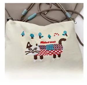 Close-up of cat and tree embroidery details on cream canvas crossbody bag with rope strap