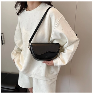 Detail of black semi-circular saddle bag with wavy flap design and gold-tone hardware