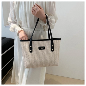 Detailed close-up of woven straw tote bag featuring black leather trim and brand label