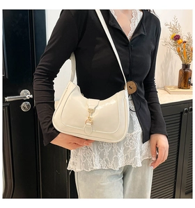 Detailed view of cream patent leather hobo bag with a golden piston clasp and curved handle