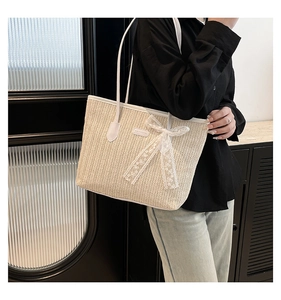 Détail d'un sac cabas en paille tissée avec nœud en dentelle blanche et anses en cuir