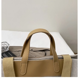 Detailed close-up of beige canvas tote bag with brown leather handles and neat stitching