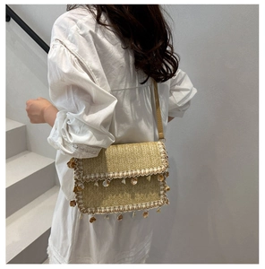 Detail of straw woven crossbody bag with shell tassels and slim shoulder strap