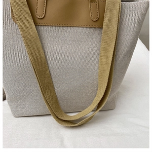 Detail view of canvas tote bag showing thick brown woven shoulder straps and leather trim