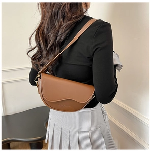 Detail view of brown leather saddle bag with wide strap and golden hardware accents