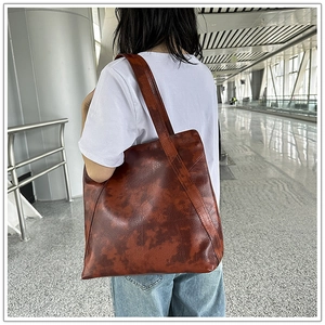 Close-up of a large brown vintage tote bag in soft leather carried by a model outdoors