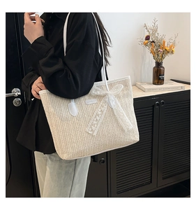 Détail du sac cabas en paille tressée avec nœud en dentelle blanche et bandoulière