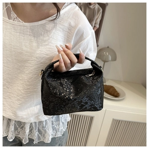 Close-up of black snakeskin texture handbag with golden zipper held by a model