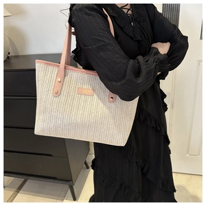 Detail of woven straw tote bag with pink leather handles and branded metal logo plate