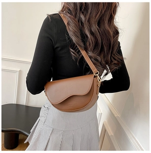 Detail view of a brown half-moon saddle bag with a unique wavy edge flap and wide strap