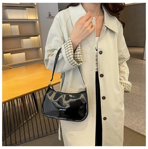 Dettaglio della borsa a tracolla in vernice nera lucida con trench coat beige