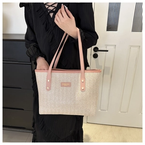 Close-up of woven straw tote bag with pink leather trim and gold brand logo plate