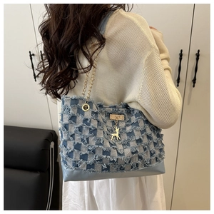 Detail of denim tote bag featuring checkered tassel texture and gold deer charm accessory