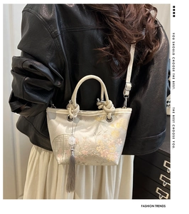 Detailed view of traditional Chinese embroidery and long tassels on a gold bucket bag