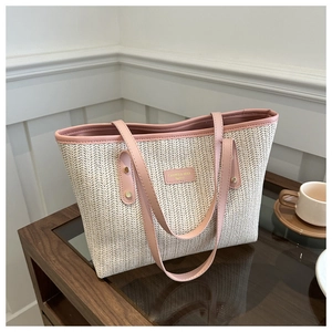 Straw tote bag with pink leather trim and metal logo on a wooden surface