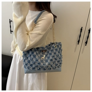 Close-up of denim patchwork tote with gold deer pendant and chain strap detail