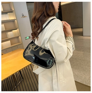 Borsa sottobraccio in pelle verniciata nera lucida indossata da una modella in biblioteca