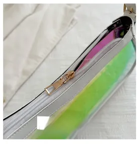 Detail of a smooth gold metal zipper on a white shoulder bag with holographic side panel