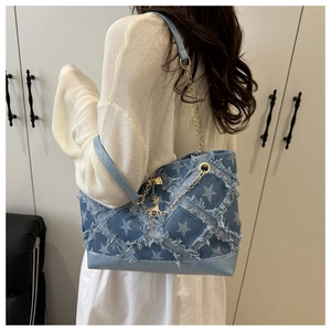 Detail of denim blue tote bag featuring star patch, raw edges and gold chain strap