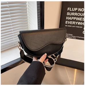 Close-up of black saddle bag with striped wide strap and fashion leather engraving