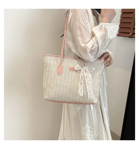 Détail d'un sac cabas en paille avec nœud en dentelle et poignées en cuir rose